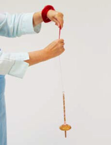person spinning on a drop spindle with fiber wrapped around their wrist